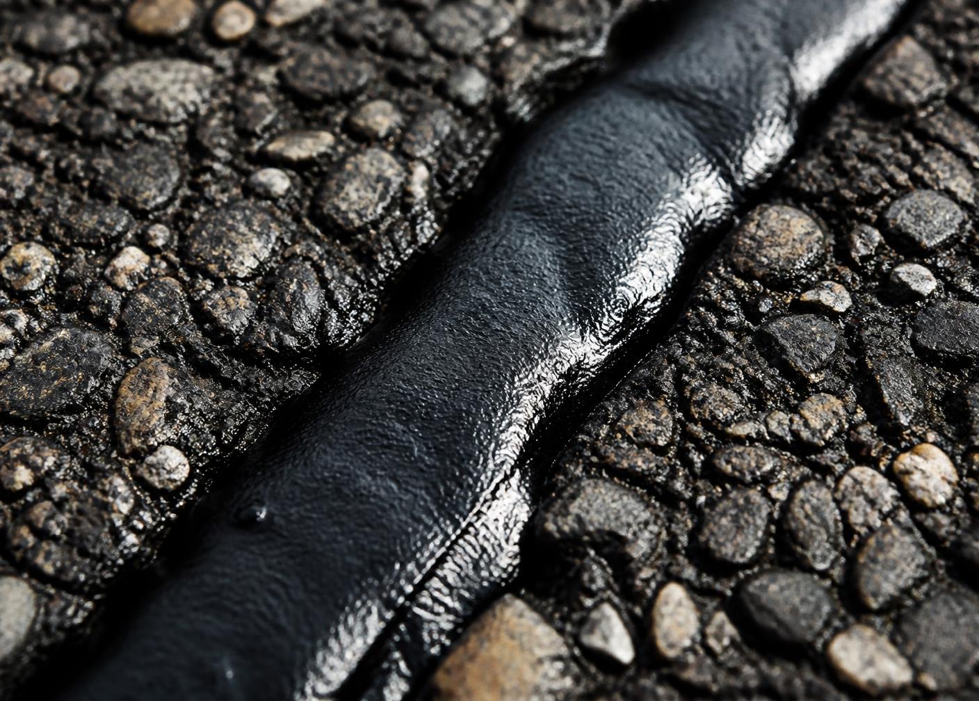 Close-up of rubberized sealant filling a crack in asphalt pavement